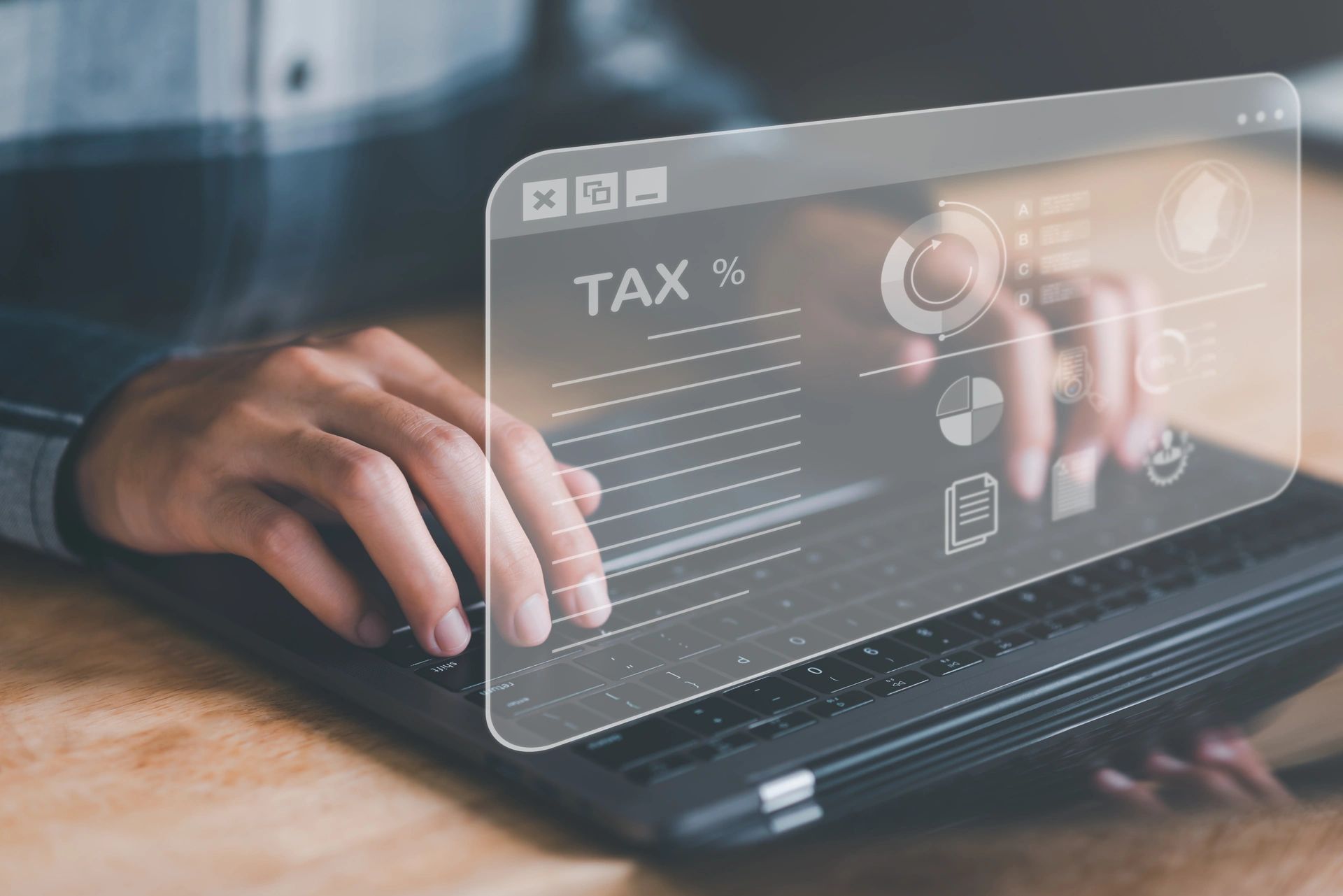 Hands typing on a laptop with a holographic display showing tax-related graphics, including pie charts, documents, and a tax percentage symbol. The display illustrates the concept of digital tax calculation and effective tax planning.